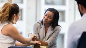 Black woman counselor holding a female client's hand with compassion during session