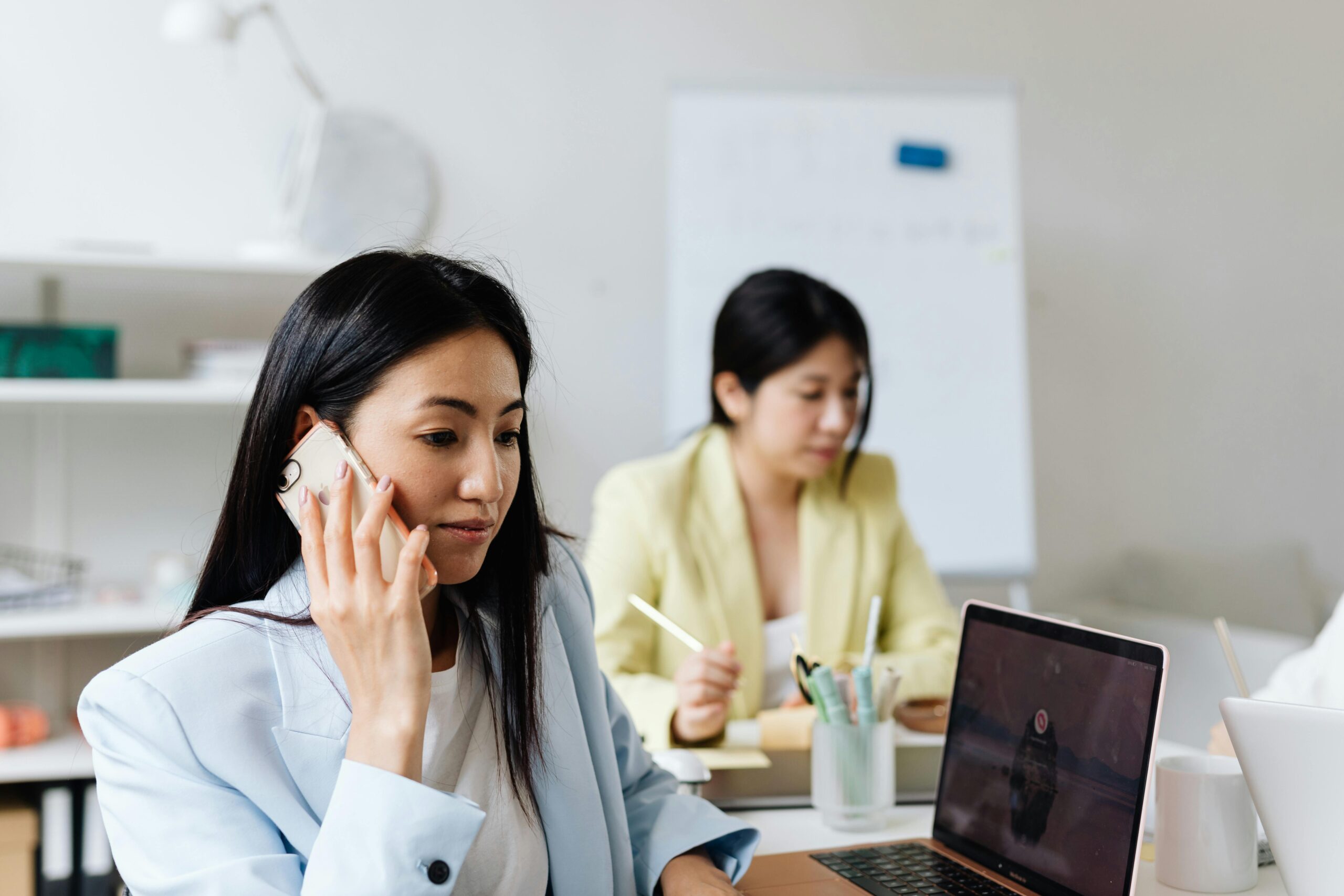 two women working on a phone and computer in an office setting